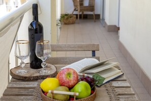 Eine Holzbank mit einer Weinflasche, Gläsern, einem Buch und einer Schüssel Obst.