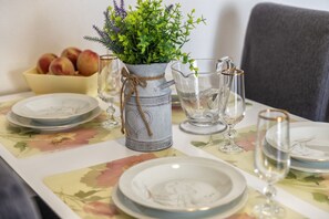Ein Esstisch mit Tellern, Gläsern, einer Karaffe und einer Blumenvase.
