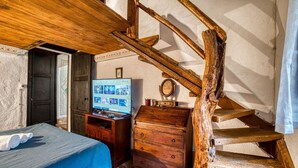 A bedroom with a wooden staircase, a bed with a blue bedspread, a wooden dresser, and a television on a wooden stand.