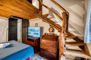 A bedroom with a wooden staircase, a bed with a blue bedspread, a wooden dresser, and a television on a wooden stand.