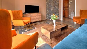 A modern living room with orange armchairs, a wooden coffee table, and a flat-screen TV.