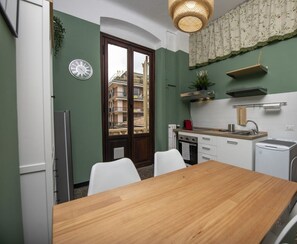 A compact kitchen with a wooden table, white chairs, a clock, and a view of a building through a glass door. - Appartamento Dalì, perfect for regenerating in Rapallo (Rapallo)