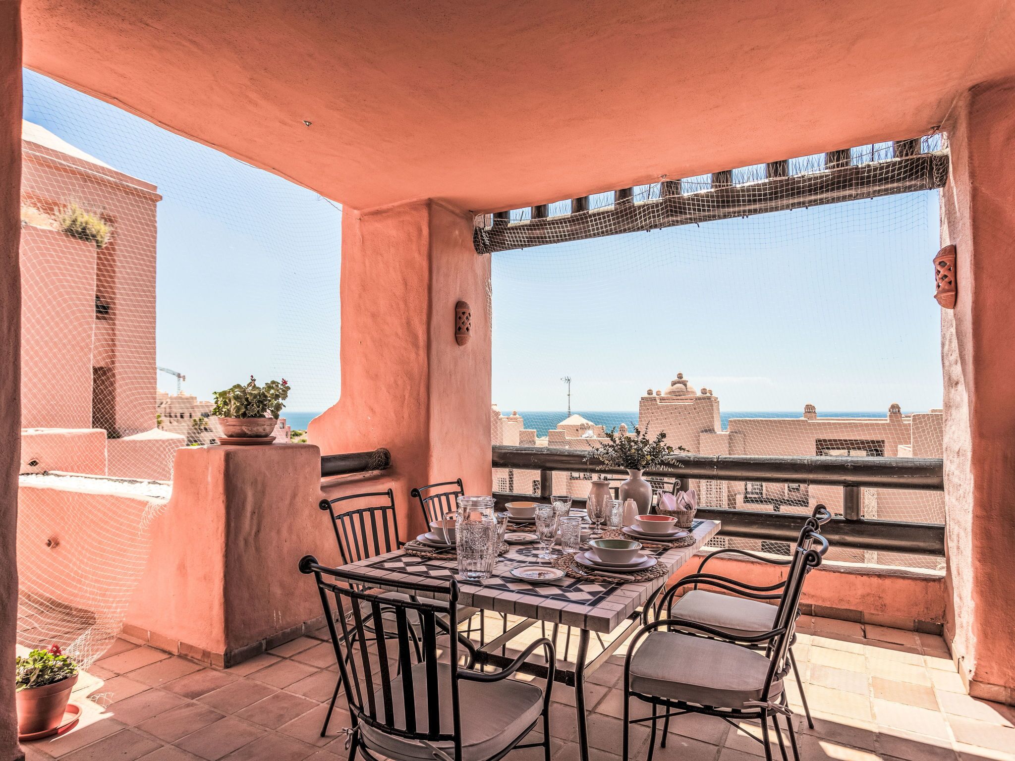 Una terraza con mesa lista para comer, sillas y plantas en macetas.