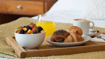A breakfast tray with a bowl of fruit, croissants, a glass of orange juice, and a cup of coffee on a woven mat.