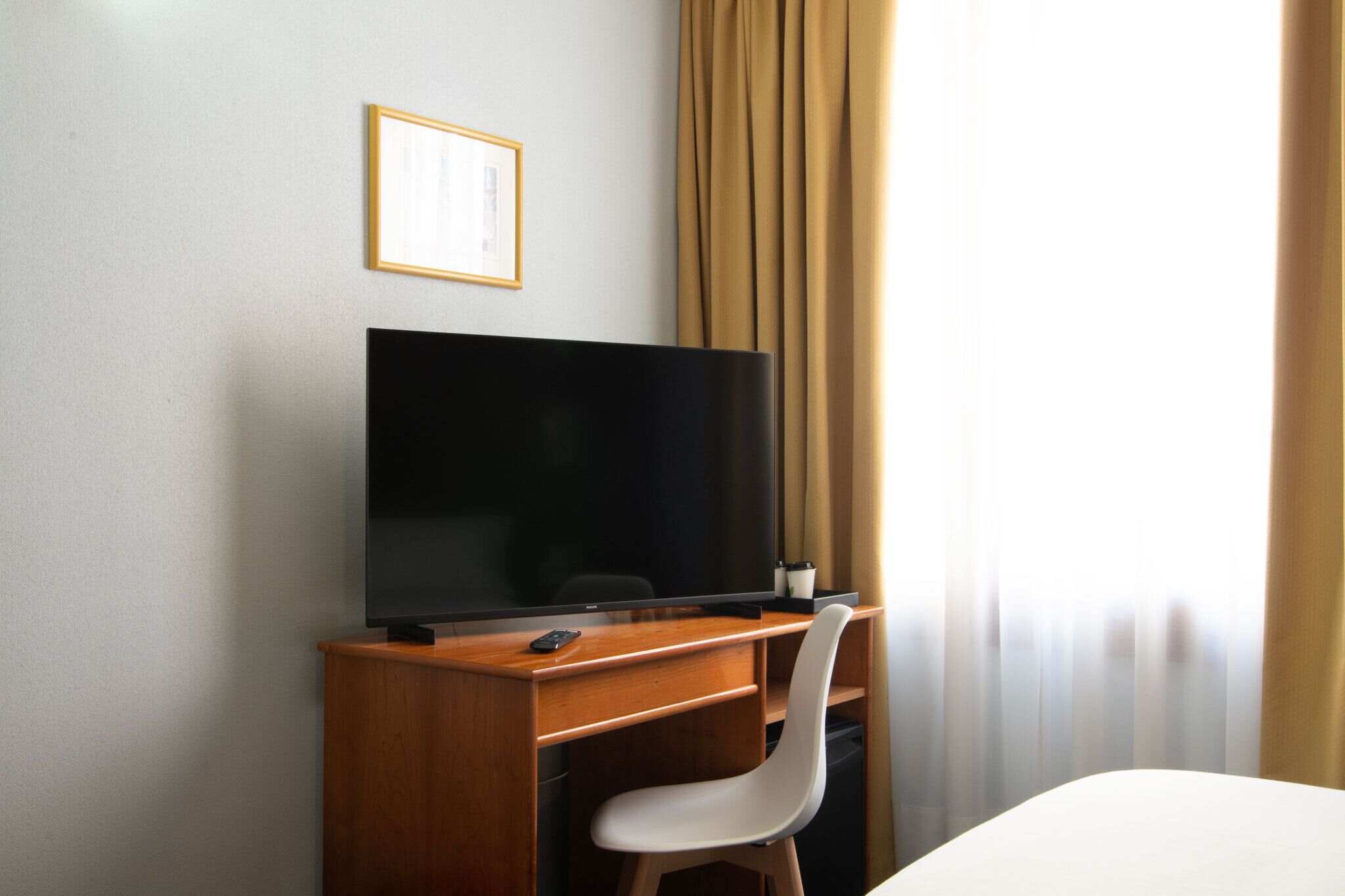 Una habitación de hotel con un escritorio de madera, una televisión, una silla blanca y una cama.