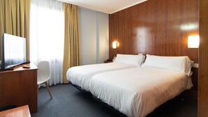 Une chambre d’hôtel avec deux lits, un bureau, une chaise et un téléviseur.