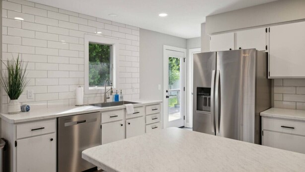 Une cuisine moderne avec des meubles blancs, des appareils en acier inoxydable et un grand îlot central.