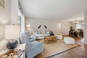 A modern living room with a sofa, striped armchair, coffee table, and a dining area with a table and chairs.