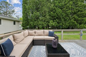 A covered outdoor seating area with a sectional sofa, a coffee table, and a decorative vase.