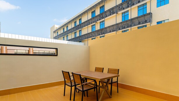 A dining area with a table and chairs, a view of a building with balconies, and a clear sky. - Ji Hotel Zhuhai Gaolangang Shopping Center (Zhuhai)