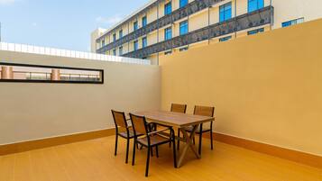 A dining area with a table and chairs, a view of a building with balconies, and a clear sky.