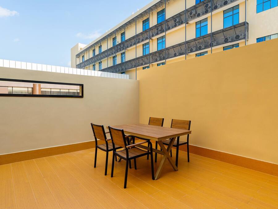 A dining area with a table and chairs, a view of a building with balconies, and a clear sky.