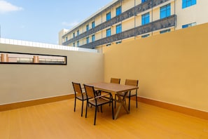 Un espace repas avec une table et des chaises, une vue sur un immeuble doté de balcons et un ciel dégagé.