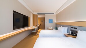 Quarto de hotel com duas camas, uma escrivaninha, uma cadeira, uma televisão e uma mesinha com telefone e uma chávena.