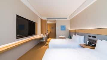 A hotel room with two beds, a desk, a chair, a TV, and a small table with a phone and a cup.