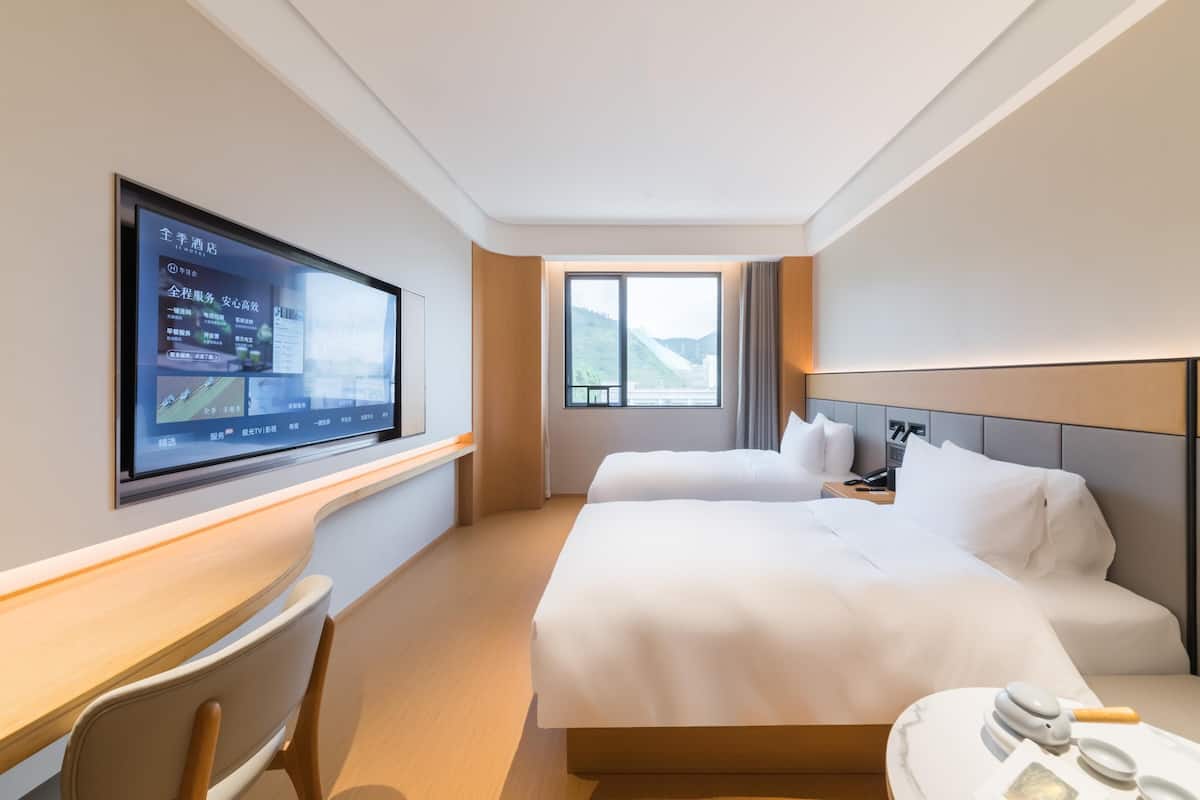 Hotellihuone, jossa on suuri sänky, työpöytä, tuoli, seinälle asennettu televisio ja ikkuna, josta avautuu näkymä vuorille.
