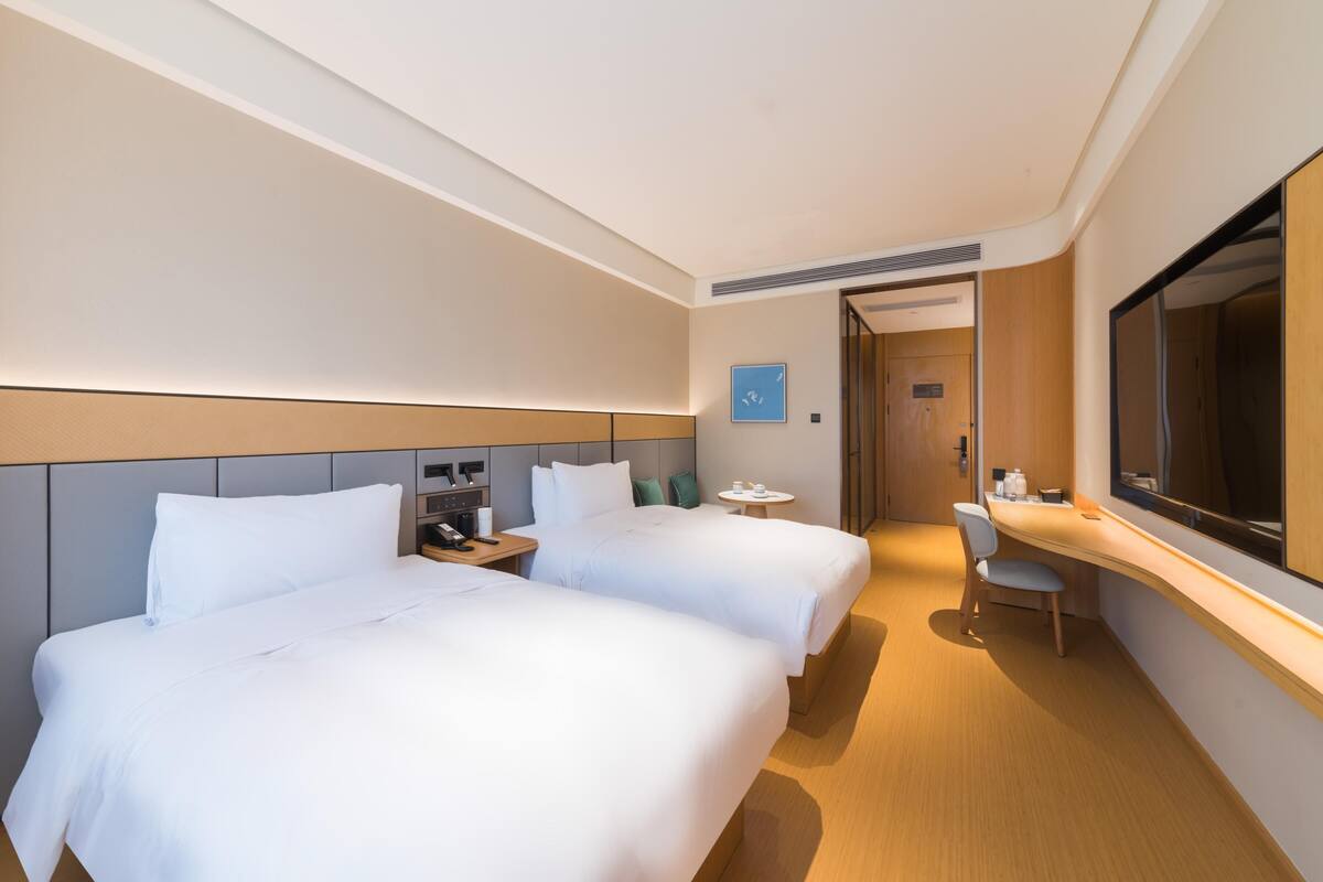 Hotellihuone, jossa on kaksi sänkyä, työpöytä, tuoli ja suuri peili.