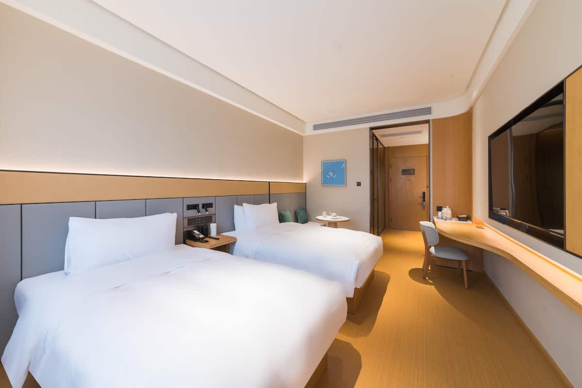Camera d'albergo con due letti, una scrivania, una sedia e uno specchio grande.