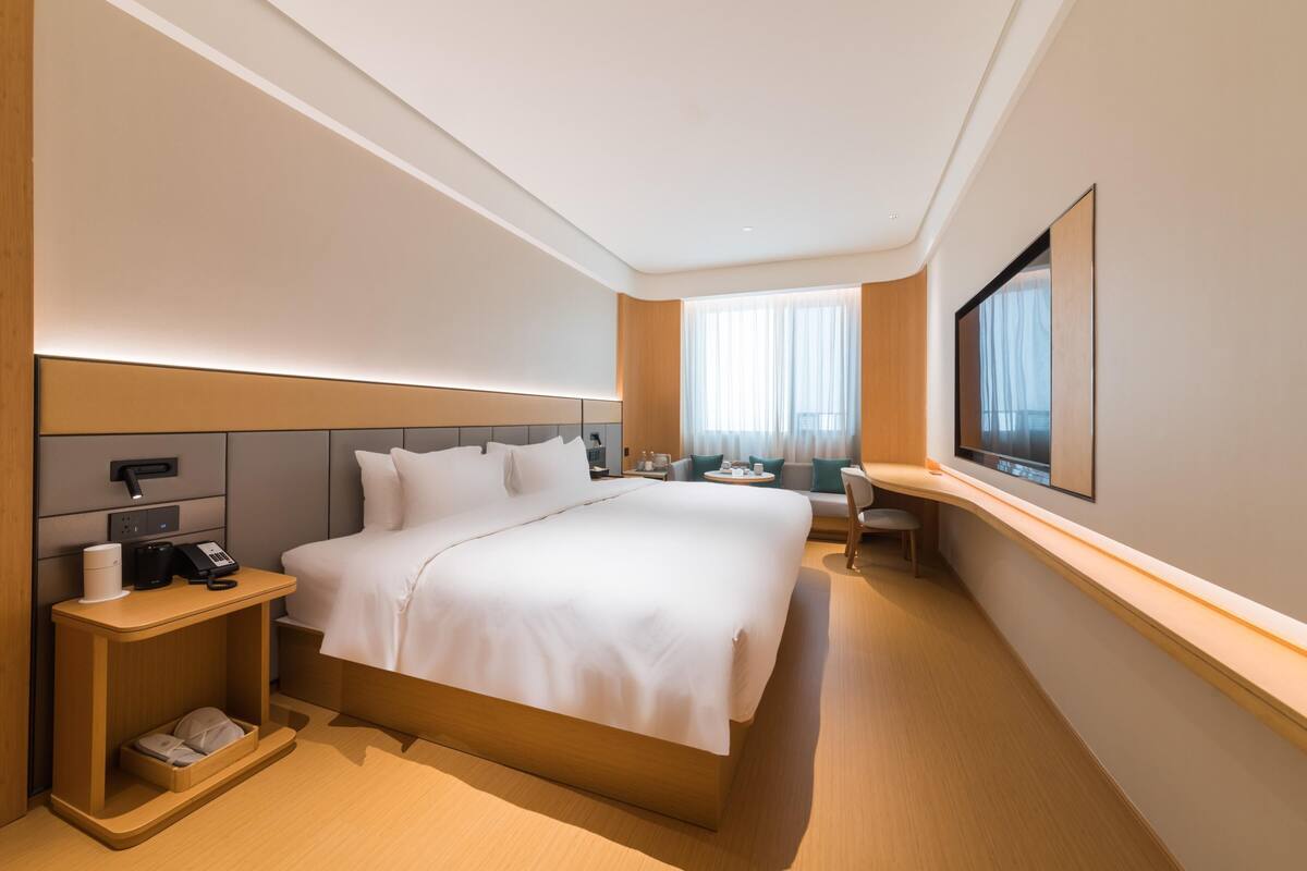 Moderni hotellihuone, jossa on suuri sänky, yöpöydät, työpöytä ja suuri ikkuna.