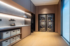 A modern laundry room with two front-loading washing machines, a countertop with toiletries, and built-in storage cabinets. - Ji Hotel Zhuhai Gaolangang Shopping Center (Zhuhai)