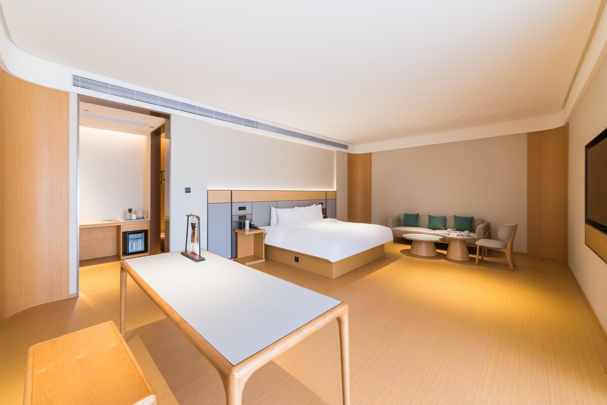A modern hotel room with a large bed, a desk, a sofa, and a TV.