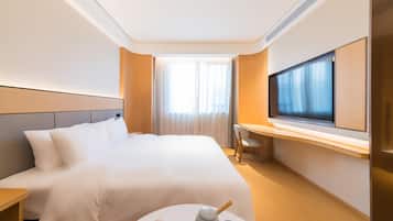 A hotel room with a large bed, a desk with a chair, a television, and a small table with a teapot and cups.