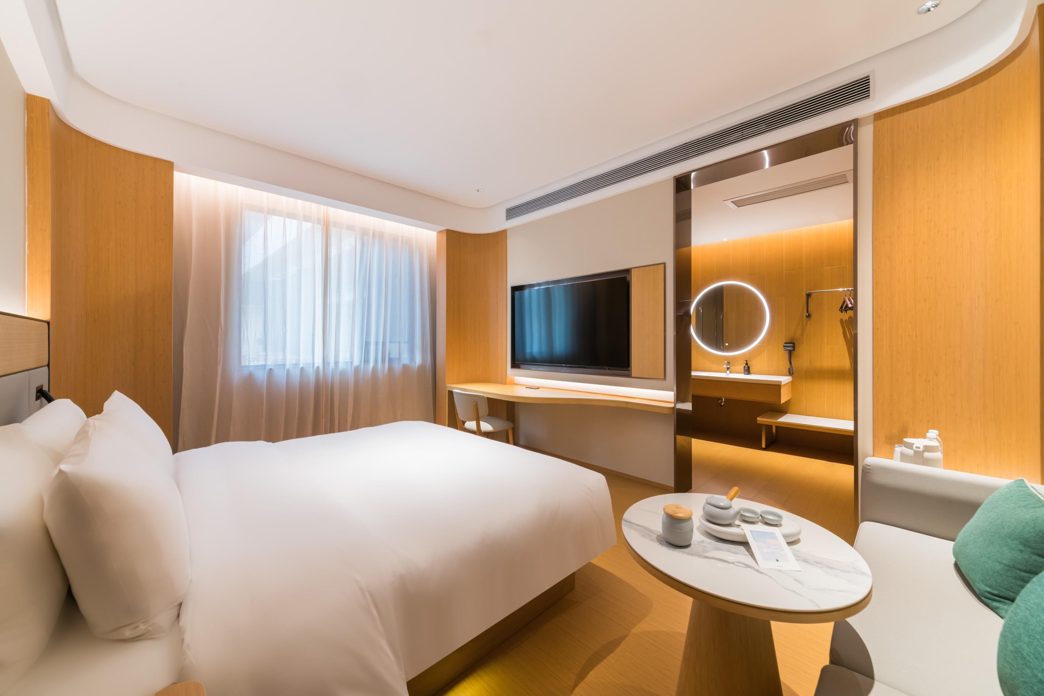 A hotel room with a bed, a desk, a television, a mirror, and a small round table with toiletries.