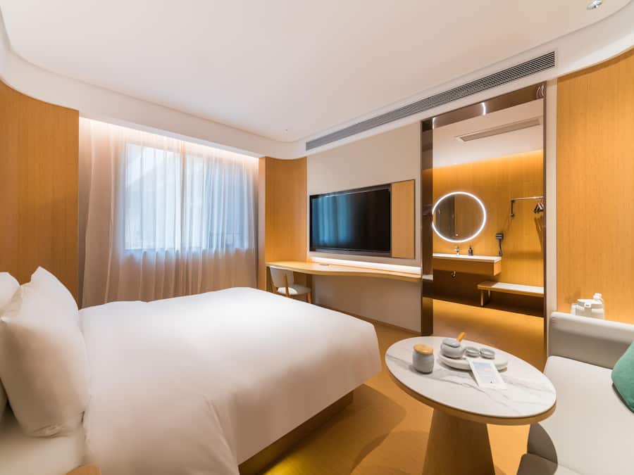 Habitación de hotel con cama, escritorio, televisor, espejo y una pequeña mesa redonda con artículos de aseo.