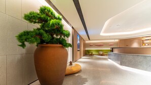 A modern hotel lobby with a large potted plant, a curved reception desk, and a seating area with wooden stools. - Ji Hotel Zhuhai Gaolangang Shopping Center (Zhuhai)