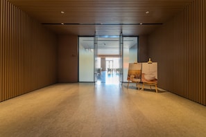 Un intérieur moderne avec un mur lambrissé en bois, une porte vitrée donnant sur un coin repas et un tableau posé sur un chevalet.