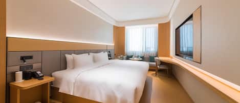 A hotel room with a large bed, bedside table, and a desk with a chair.
