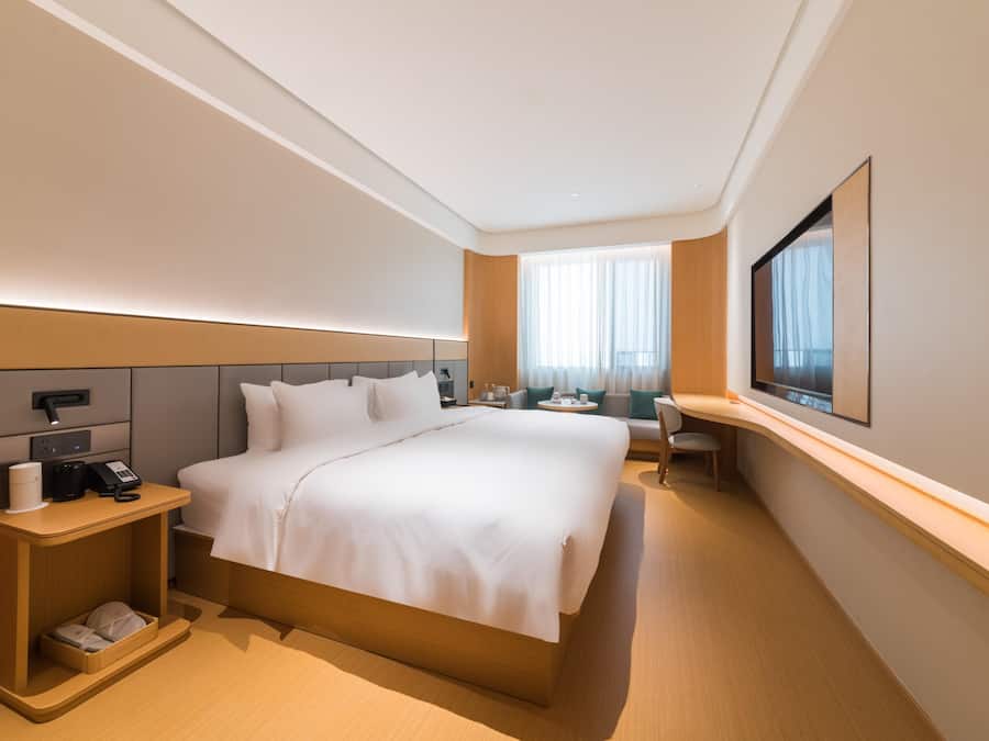 A hotel room with a large bed, bedside table, and a desk with a chair.