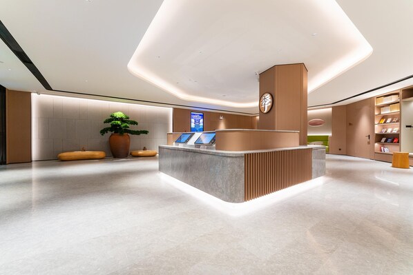 A reception desk with a digital screen, a potted plant, and a wooden bench. - Ji Hotel Zhuhai Gaolangang Shopping Center (Zhuhai)