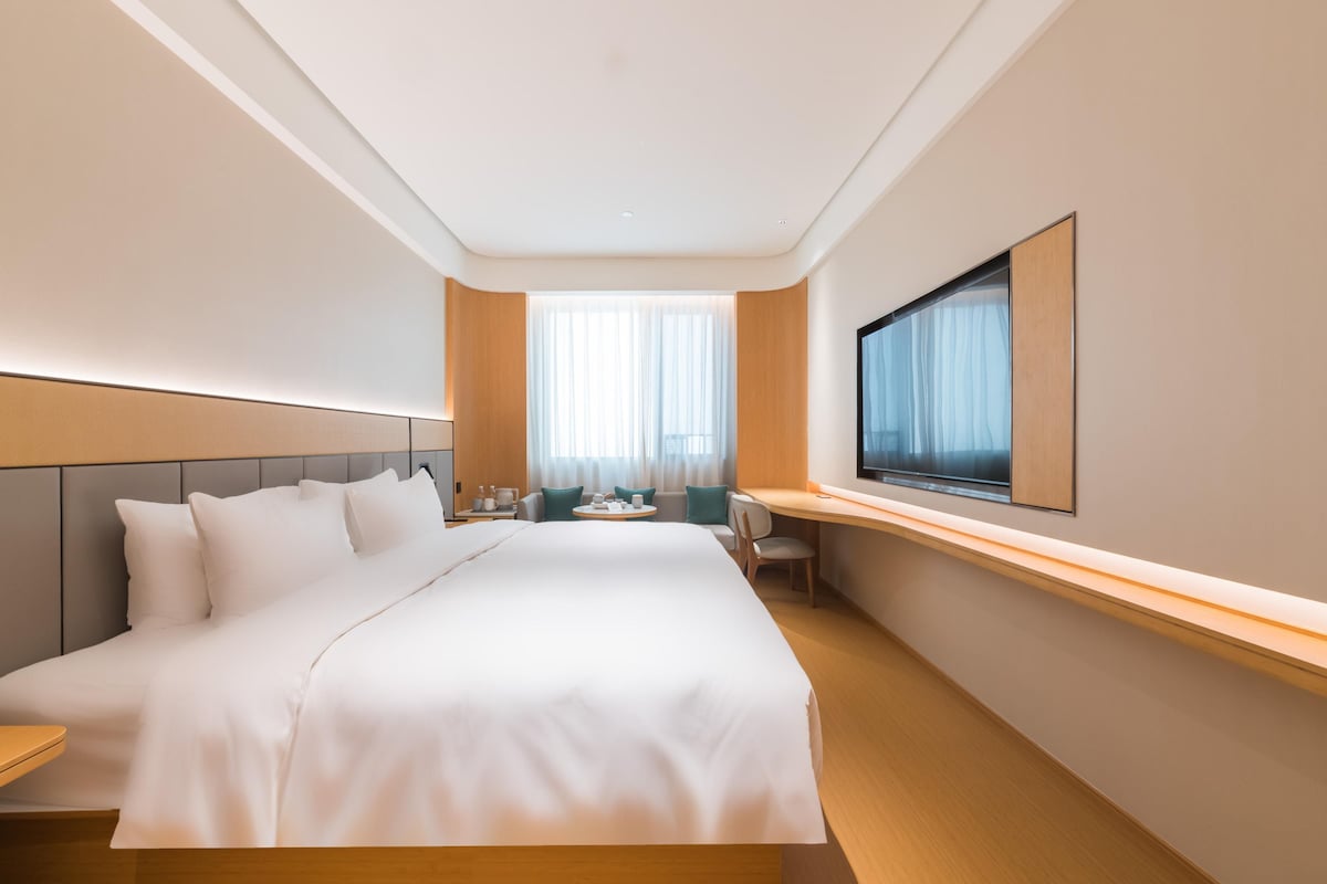 A hotel room with a large bed, a desk, a chair, a TV, and a window with curtains.