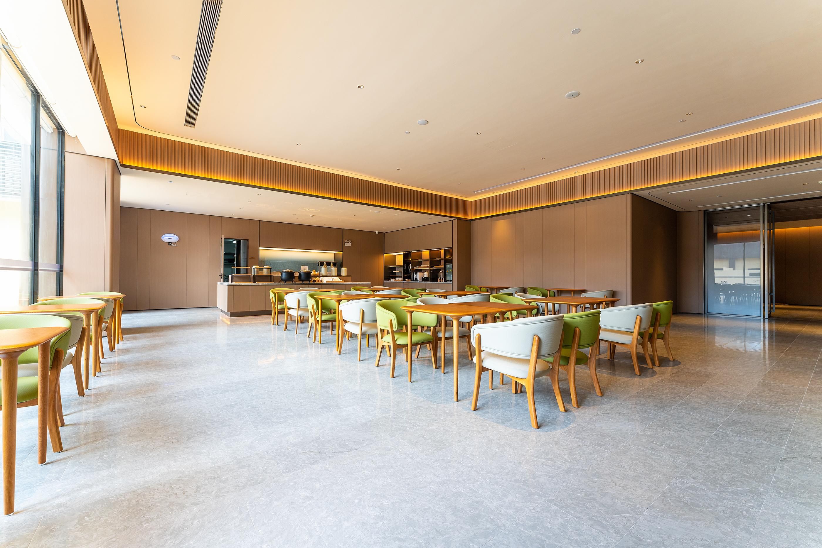 Un comedor amplio con varias mesas y sillas, una cocina al fondo y un diseño de techo moderno.