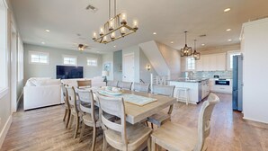 A spacious living area with a dining table, chairs, and a sofa. There is a kitchen area with modern appliances and a large island. - Private Pool, Golf Cart Included, Parking for 4 (Port Aransas)
