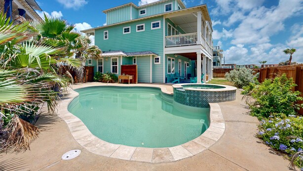 A two-story house with a swimming pool, surrounded by tropical plants and a wooden fence. - Private Pool, Golf Cart Included, Parking for 4 (Port Aransas)