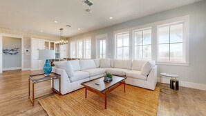 A spacious living room with a large sectional sofa, a coffee table, and a rug. There are large windows providing natural light and a view of the outdoors. - Private Pool, Golf Cart Included, Parking for 4 (Port Aransas)