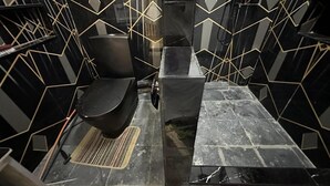 Een kamer met een zwart en goud geometrisch tegelpatroon op de muren, een zwarte bank en een tafel met metalen frame.