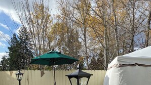 An outdoor patio area with a table and chairs, a green umbrella, and a white tent. - CALM Guest House (Auburn)