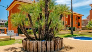 A building with a tiled roof and a circular wooden planter with palm trees.