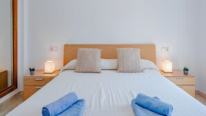 A neatly made bed with two pillows, two bedside tables with lamps, and a mirror on the left.