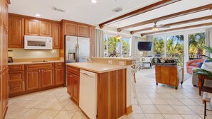 A spacious kitchen with wooden cabinets, a central island, and a large window overlooking a tropical landscape. - Beachfront Condo w Ocean Views and Pool (Tybee Island)