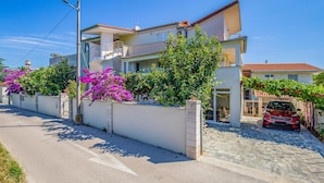 Une maison à deux étages avec un balcon, une allée pavée et une voiture garée.