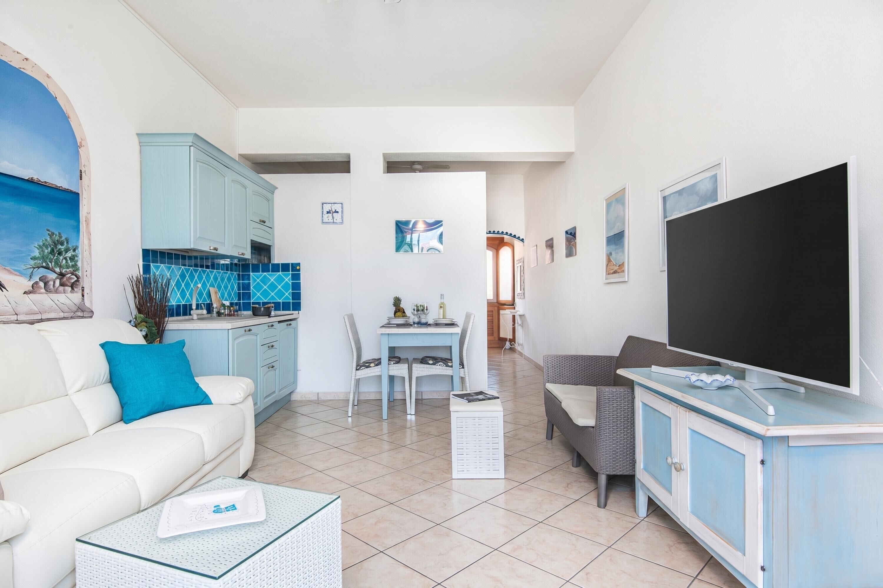 Una sala de estar con sofá, mesa de centro, televisor, comedor con sillas y cocina con armarios.