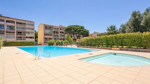 Un espace piscine avec un sol carrelé, un plongeoir et, au fond, un bâtiment doté de plusieurs balcons.