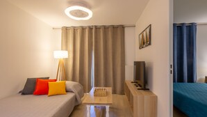 Une chambre d’hôtel avec un lit, une table de chevet, une lampe, un téléviseur et une vue sur l’extérieur par une fenêtre munie de rideaux.