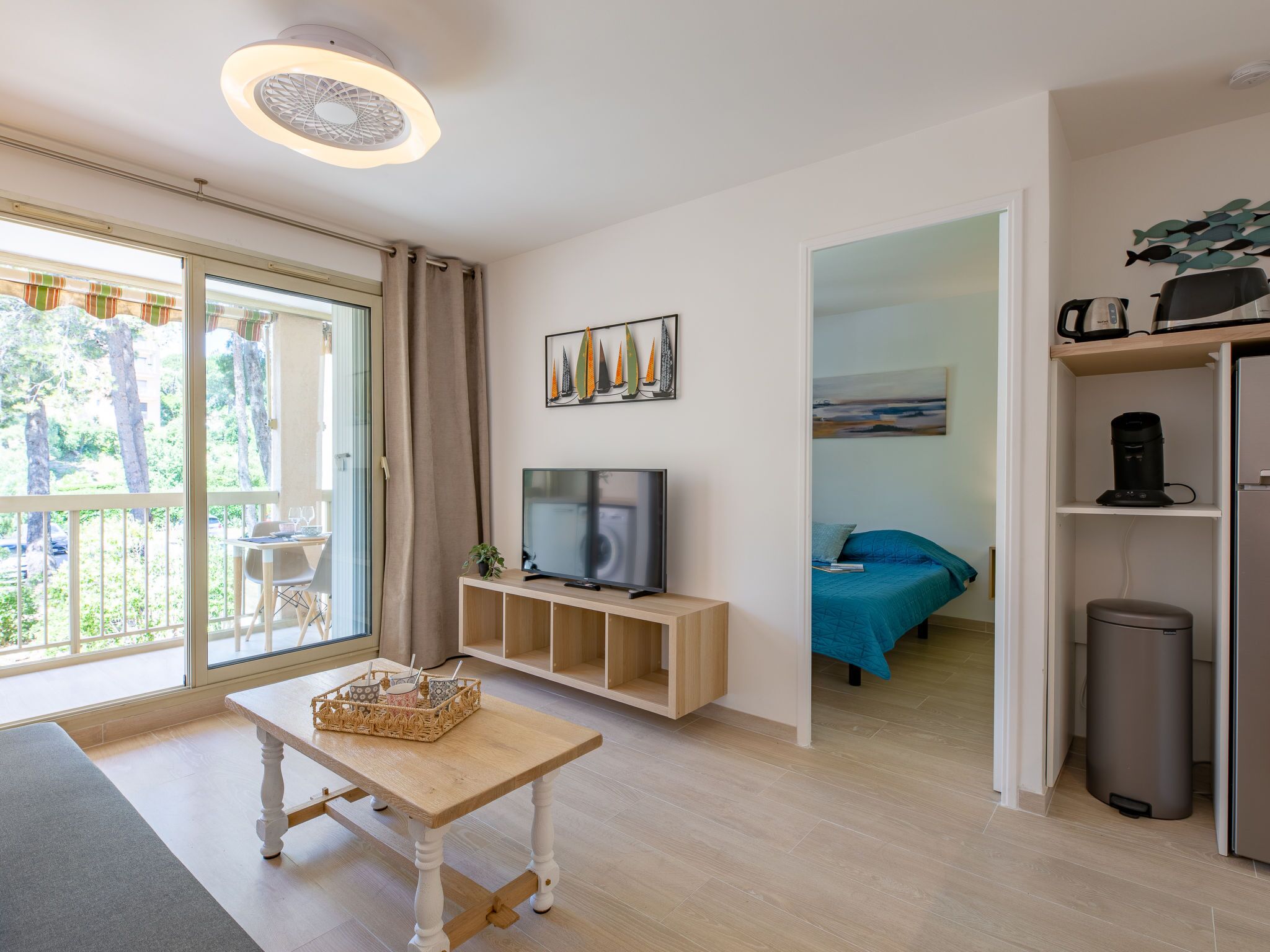 Una sala de estar moderna con televisor, una mesita y un balcón con vista a árboles.
