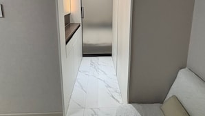 Ein schmales Entree mit Marmorboden, einer eingebauten Bank rechts und einer eingelassenen Deckenleuchte.