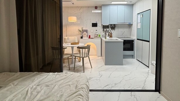 Ein modernes Hotelzimmer mit einem Bett, einem Essbereich mit Tisch und Stühlen, einer Küche mit Schränken und Geräten sowie einem Badezimmer mit Toilette und Waschbecken.